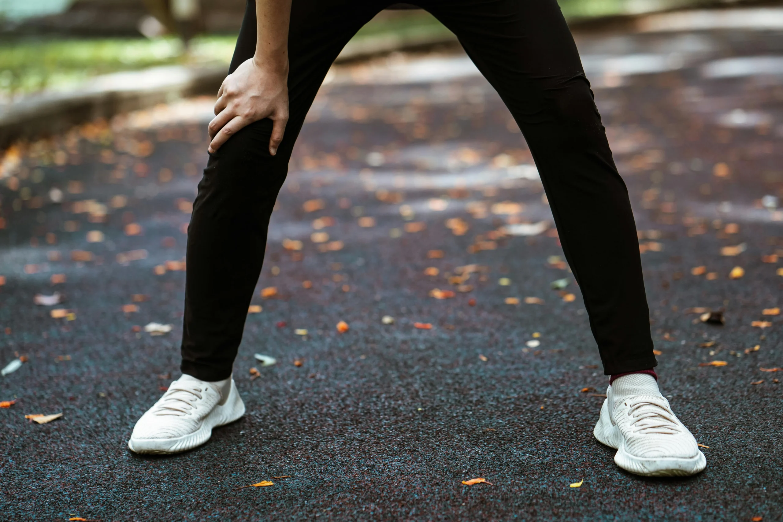 zwarte trainings broek en witte hardloopschoenen van een persoon die staat uit te heigen na het hardlopen